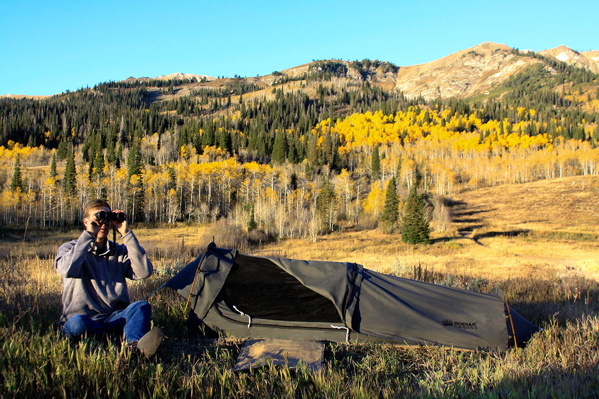 Outdoor camping tent in green, set against autumn scenery with a person using binoculars.