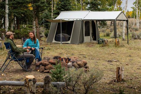 Outdoor camping scene with a large olive green tent, couple by a campfire, surrounded by trees.