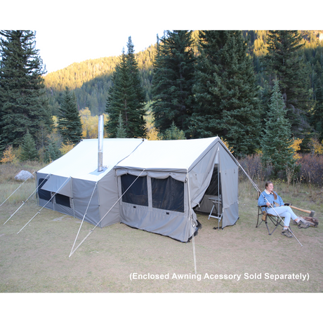 Another lifestyle image of the cabin lodge tent in the woods - this image is shown with the optional awning enclosure attached, and a woman sitting in a chair in front of the tent.