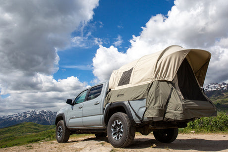 Gray pickup truck with a beige rooftop tent, ideal for camping in scenic mountainous areas.