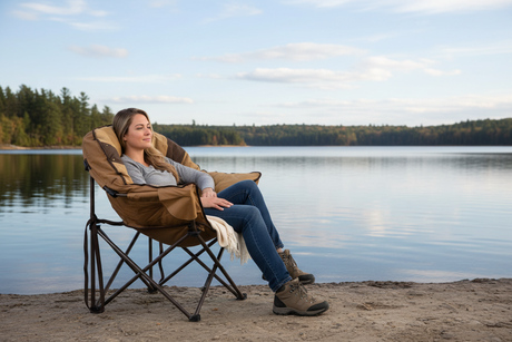 Comfortable brown camping chair by the lake, featuring a relaxed woman wearing gray top and jeans.
