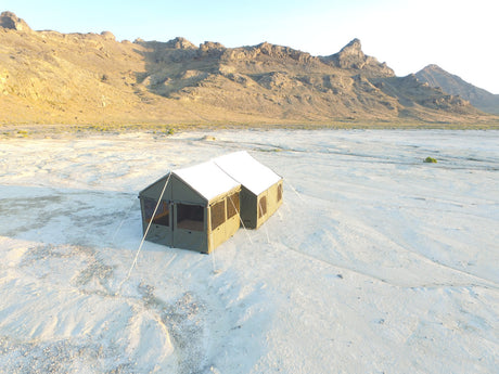 Spacious green canvas camping tent with white roof, set in a desert landscape for outdoor adventures.