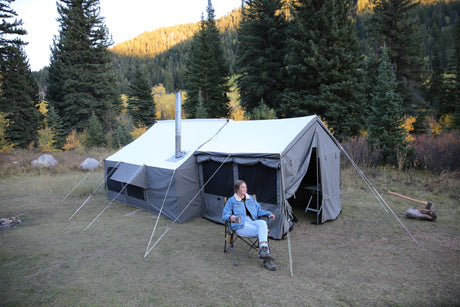 Spacious beige camping tent with wood stove pipe, perfect for outdoor adventures, surrounded by trees.