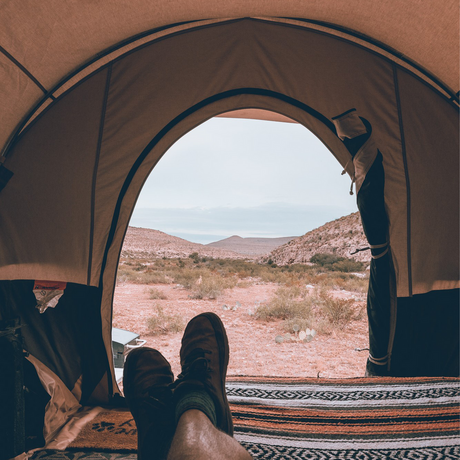 Cozy tent interior view with brown boots, overlooking a desert landscape and mountains.