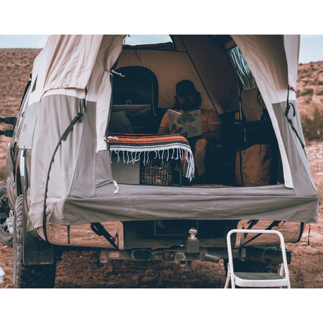 Gray truck tent setup with cozy interior, featuring a blanket, books, and camping essentials.