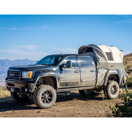 Black GMC truck with tent, off-road tires, parked in a mountain landscape for camping adventures.