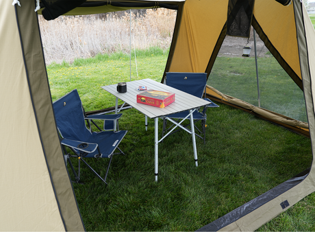 Cozy camping setup with blue folding chairs and a portable table under a tent in a grassy area.